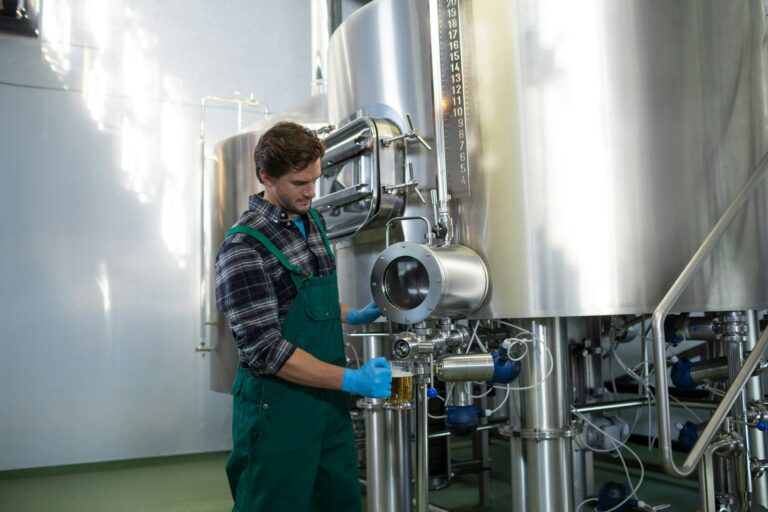 Male worker taking beer from storage tank at factory